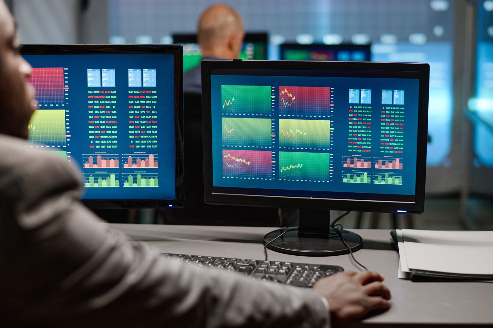 Analyst Working With Graphs And Charts. Rear view of modern African American broker sitting in front of computer monitors watching and analyzing previous stock trading stats in evening
