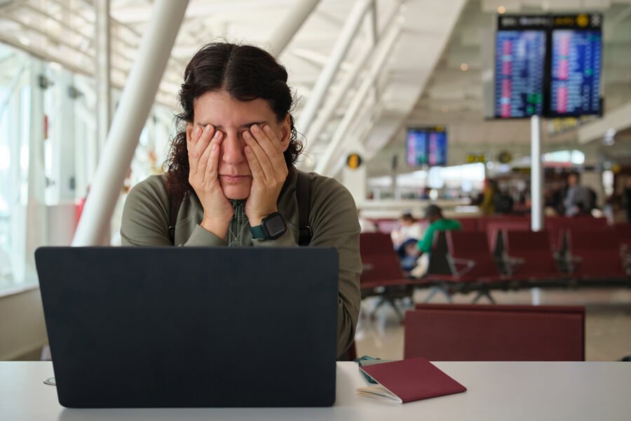 Tired woman suffering jet lag at airport waiting lounge Woman covering her eyes at airport gate, exhausted from long travel, jet lag and delays while working on laptop and waiting to depart