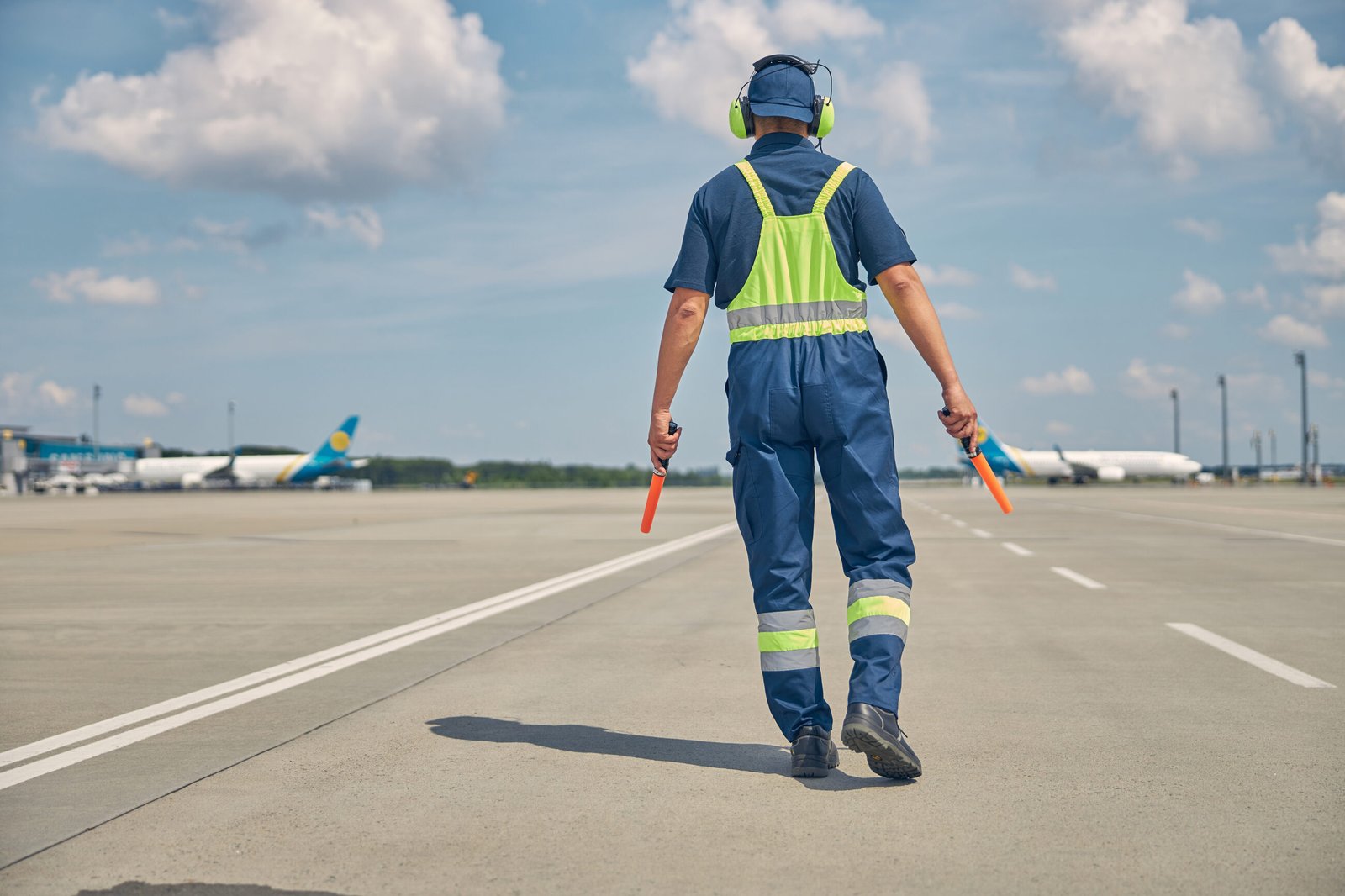 Back view of a male in uniform and noise-canceling headphones walking towards the landed planes. HR Business Partners