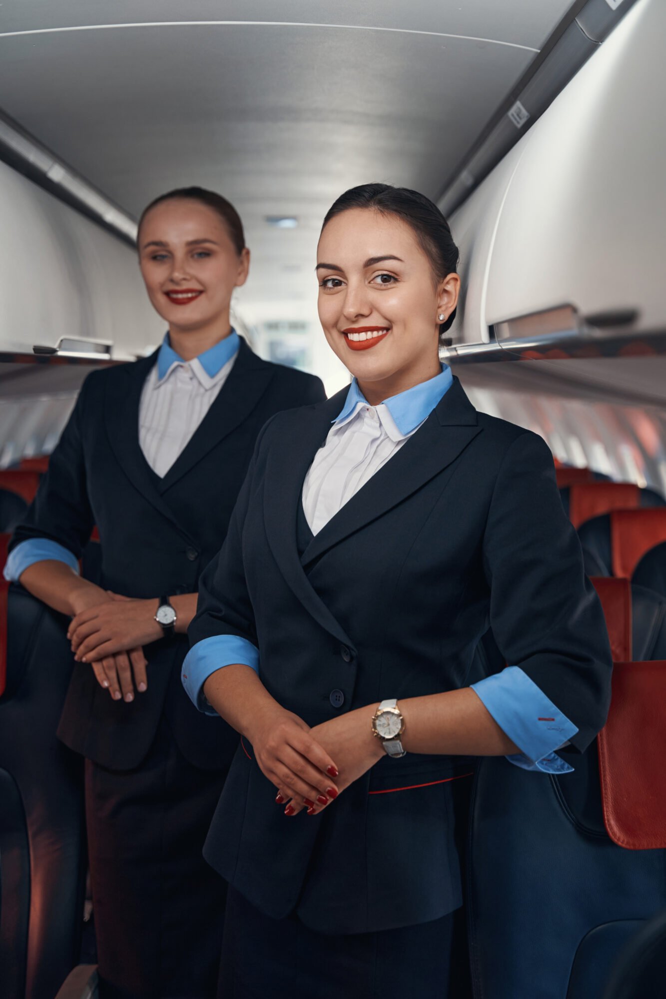 Two stewardesses standing on airplane aisle with folded hands. HR Business Partners