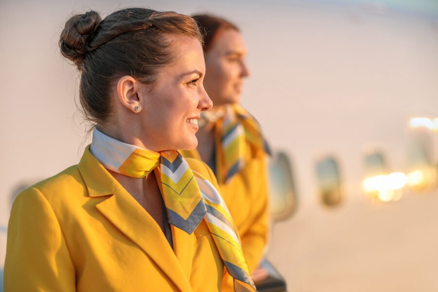 Joyful woman stewardess with air hostess scarf on her neck looking away and smiling while standing beside her colleague. Employee retention in aviation