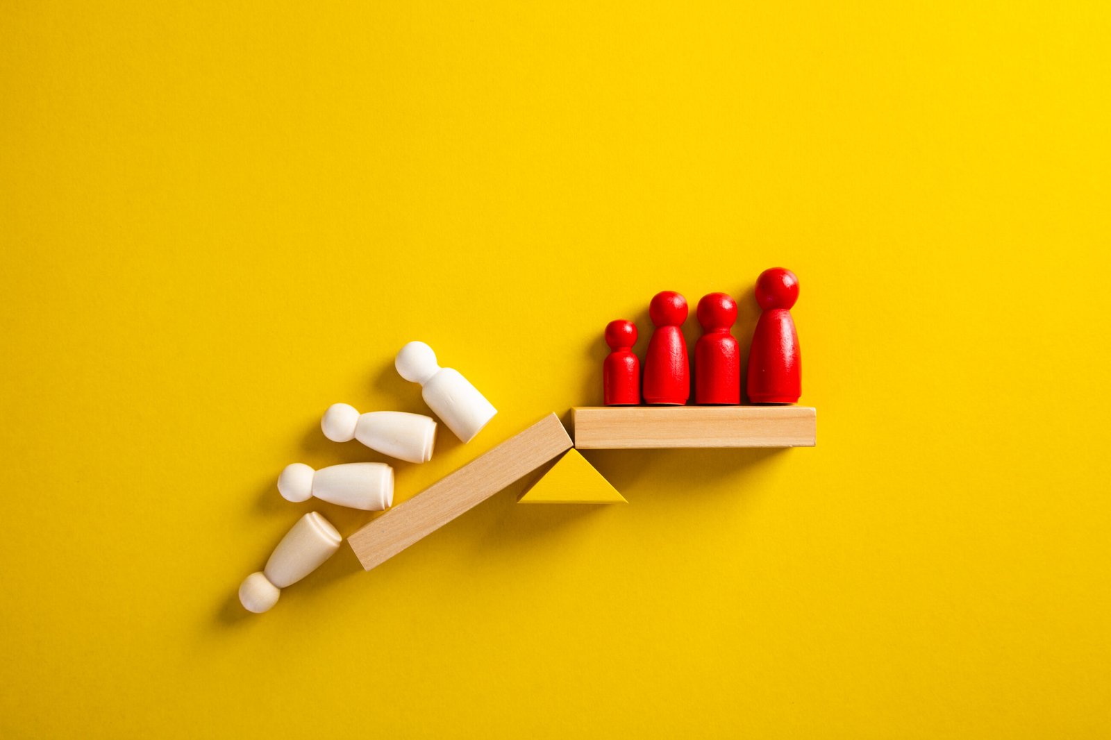 Balance of power represented by red and white wooden figures on a seesaw.