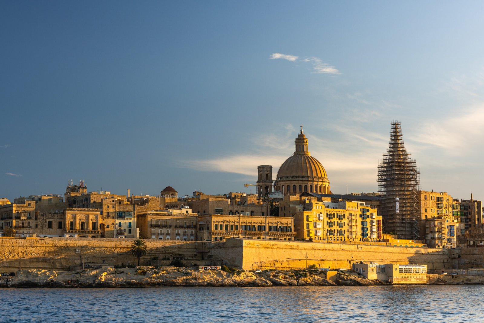 Valletta skyline and historic buildings viewed from across the water at sunset.